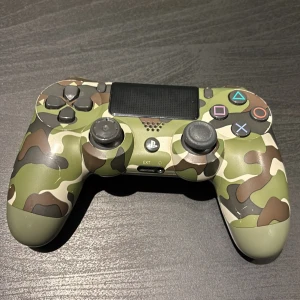 Sony DualShock 4 Camouflage Edition - Snygg Sony DualShock 4 trådlös handkontroll i camouflage-design för PlayStation 4. Kontrollen är i gott skick med mindre slitage på styrspakarna, alla knappar och funktioner fungerar. Perfekt för dig som vill ha en unik och pålitlig spelupplevelse.