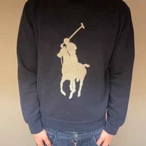  Sweatshirt Polo Ralph Lauren - Snygg mörkblå sweatshirt från Polo Ralph Lauren med stort broderat Ralph lauren märke i vitt på bröstet. Tröjan har rund halsringning, långa ärmar och är tillverkad i mjuk bomull. 