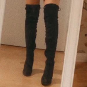Svarta overknee stövlar med klack - Säljer ett par svarta overknee stövlar med hög klack och rund tå. Stövlarna är tillverkade i mjuk mocka och har en stilren, slimmad passform som går över knäna 