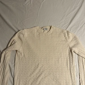 Beige stickad tröja från Selected Homme - Snygg beige stickad tröja från Selected Homme i storlek M. Tröjan har ett klassiskt kabelstickat mönster, rund hals och långa ärmar. Perfekt för dig som gillar stilrena och tidlösa plagg med skön passform.