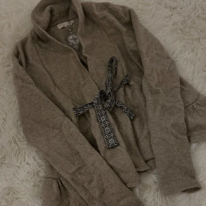 Beige kofta med knyt från Odd Molly - Supermysig beige kofta från Odd Molly med broderad kompass på ryggen och insidan. Koftan har långa ärmar med volangdetalj och ett snyggt mönstrat knytband i midjan. Perfekt för lager-på-lager och chill dagar. Använda 2 gånger. Pris:250kr super fin och skön! Storlek xs/s 