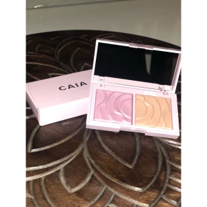 CAIA highlighter duo i rosa och guld - Highlighterpalett från CAIA med två skimrande nyanser: en ljusrosa och en varm guld. Kommer i en snygg ljusrosa ask med spegel i locket. Pressat puder med vågigt mönster, perfekt för att ge glow till ansiktet.