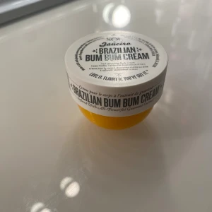 Sol de Janeiro Brazilian Bum Bum Cream 25ml - Ej använd. Sol de Janeiro Brazilian Bum Bum Cream i en rund, gul plastburk med vitt lock. Kroppskrämen är snabbt absorberande och innehåller guaranaextrakt. Perfekt för dig som vill ha en tropisk doft och mjuk hud. Förpackningen är smidig att ta med i väskan.