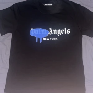 Palm Angels svart t-shirt New York - Svart t-shirt från Palm Angels med ikoniskt New York-tryck framtill. Stor blå drip-effekt över loggan ger en streetstyle vibe. Klassisk rund hals och korta ärmar. Skön bomullskvalite men liten i storlek.