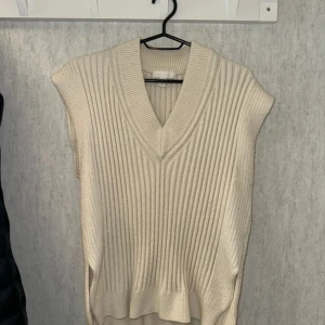 Ribbad stickad väst i beige - Snygg beige stickad väst med bred v-ringning och ribbad struktur. Västen har en loose passform och är perfekt att styla över en skjorta eller t-shirt. Fint använd skick / lite nopprig storlek xs