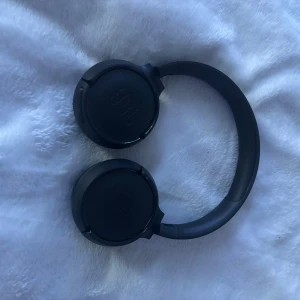 JBL Tune 500BT - JBL Tune 500BT trådlösa on-ear hörlurar i svart. Lätta och bekväma med tydlig JBL Pure Bass-ljudprofil. Synligt i gott skick utan större repor eller slitage. Perfekt för musik och samtal med lång batteritid och enkel Bluetooth-anslutning.