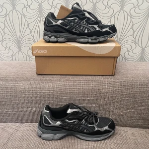 Svarta och silver Asics sneakers - Snygga Asics sneakers i svart och silver med coola detaljer och grå sula. Skorna har meshpaneler för extra andningsförmåga, syntetiska och mockaliknande partier samt klassisk snörning. Perfekta för dig som gillar sportig och modern stil.