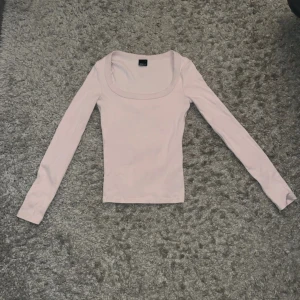 Ljusrosa långärmad topp Gina Tricot - Supersöt ljusrosa långärmad topp från Gina Tricot med rundad, bred urringning. Toppen är ribbad och har en slim passform som sitter snyggt på kroppen. Perfekt att styla med jeans eller kjol för en clean look.