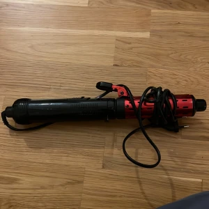 Elektrisk locktång - Elektrisk locktång med svart och röd design, synligt sladd och klämma. Produkten  är i gott skick utan synliga defekter eller slitage. Perfekt för att skapa lockar och volym i håret. Enkel att använda och passar de flesta hårtyper.