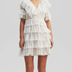 Vit spetsklänning från By Malina - Supersöt vit kortklänning från By Malina med flera lager volanger och v-ringning. Klänningen har korta ärmar och är täckt av spets. Väldigt fint skick och använd endast en gång. Nypris 2800 kr