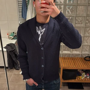 Mörkblå stickad kofta från Stenströms - Säljer en mörkblå stickad kofta från Stenströms i storlek S. Koftan har grovstickad struktur, bred sjalkrage och knäpps med fem knappar framtill. Perfekt för lager-på-lager och chillare dagar.