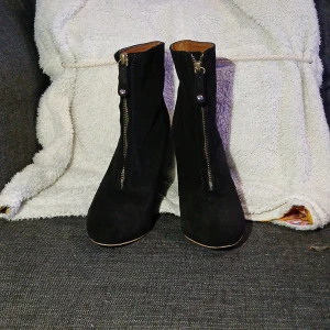 Svarta kilklacksstövletter från ZARA - Snygga svarta stövletter med kilklack och rund tå. Utsidan är i mocka och insidan har ett brunt foder. Dragkedja framtill med dekorativ detalj. Perfekt för dig som gillar boots med lite höjd och stilren look. Lite slitage på insidan men har mycket att ge dig. Storlek är 39 men jag är 39 och de passar inte på mig då skulle jag säga att de passar bra i stlk 38.