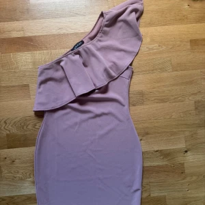 Rosa one shoulder klänning Parisian - Säljer en snygg rosa kortklänning från Parisian med one shoulder-design och bred volang över axeln. Klänningen har en figurnära passform och är tillverkad i ett mjukt, stretchigt material som sitter skönt på kroppen. Perfekt för dig som vill sticka ut lite extra!