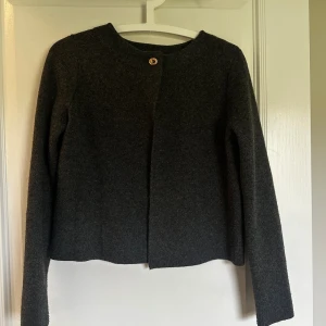 Mörkgrå ulljacka från Zara - Mörkgrå, stilren kofta från Zara i ullblandning. Modellen är rak och kortare med rund halsringning och en dekorativ guldig knapp framtill. Perfekt för dig som gillar minimalistisk och clean stil.