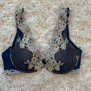 Intimissimi bh - Supersnygg mörkblå bh med transparent mesh och beige broderade blommor längs axelbanden och kuporna. Blusen har spetsdetaljer och ett elegant blommigt mönster. Använt få tal gånger, det syns att jag har använt den men inga täcken på slitning! 