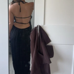 Svart långklänning med öppen rygg - Säljer en svart långklänning med halterneck och snygg öppen rygg med tunna band. Klänningen har en figurnära passform och faller snyggt längs kroppen. Perfekt för dig som vill ha en stilren och elegant look.