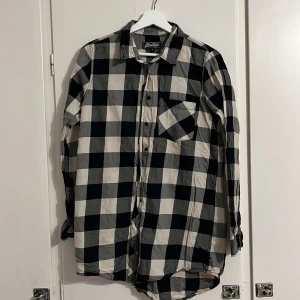 Rutig skjorta från Miss Milla S - Svart och vit rutig skjorta från Miss Milla i storlek S. Klassisk modell med lång ärm, bröstficka och knappar framtill. Skjortan har en loose passform och är tillverkad i mjuk bomull, perfekt för en avslappnad look.