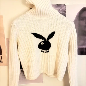 Vit polotröja med Playboy-logo - Vit ribbstickad polotröja från Playboy med svart ikonisk kaninlogo framtill. Tröjan har hög polokrage, lång ärm och är gjord i mjukt stickat material. Perfekt för dig som vill ha en statement piece med cool vibe.