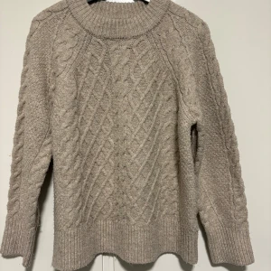 Beige stickad tröja från 157 XS - Säljer en beige stickad tröja från 157 i storlek XS. Tröjan har ett snyggt kabelstickat mönster framtill och på ärmarna, samt bred ribbad krage och muddar. Perfekt för dig som gillar mysiga och klassiska vibes.(använt några få gånger) priset kan diskuteras.