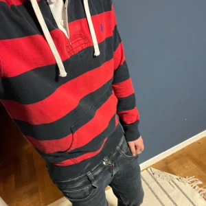 Randig hoodie från Polo Ralph Lauren - Säljer en snygg hoodie från Polo Ralph Lauren med breda röda och mörkblå ränder. Tröjan har huva med vita snören, känguruficka och lång ärm. Broderad blå logga på bröstet och knappslå vid halsen. Perfekt för chill dagar. Passar till det mesta riktigt fett inga defekter jag har märkt, Brq skicka skulle jag säga men bedömer självklart själv ut efter bilder skriv vid minsta fundering🌟