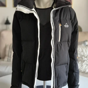 SOS * Svart dunjacka * Stl 42 - Svart dunjacka från SOS Sportswear of Sweden.  Jättefint skick!! Alla fickor, dragkedjor mm är kollade. Storlek 42, sann i storleken.  Se mått bland foton & fråga om du inte kan tyda dem. Flera fickor med dragkedja och två innerfickor.  Putsduk & mjukt glasögonfodral i bröstfickan. Säkerhetsrem för mobil, nycklar etc i ena sidofickan. Hög och vadderad krage Inbyggd mudd i ärmarna  80/20 dun/fjädrar  Dragsko i kragen och ryggslut.