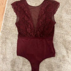 Vinröd spetsbody från Pieces - Säljer en vinröd body från Pieces i storlek S. Bodyn har spetsdetaljer framtill, meshpartier och djup v-ringning. Ärmlös design med fina spetskanter vid axlarna. Perfekt att styla med jeans eller kjol för en cool look.