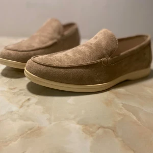 Beige mockaloafers från Old Money - Snygga loafers i beige mocka från Old Money. Skorna har en klassisk, rund tå och platt sula i ljus ton. Perfekt för dig som gillar stilrena och tidlösa detaljer. Mjukt material och enkel slip-on design gör dem superbekväma. I princip oanvända men saknar boxen de låg i. Originalpris 1000kr. Rabatt vid beställning med postnord. 