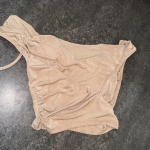 Beige linne med glittrig yta från SHEIN - Snygg beige linne från SHEIN i storlek M. Linnet har en glittrig finish och är designad med snygga rynkade detaljer och en axelrem. Perfekt för dig som vill sticka ut på natten med en trendig look.