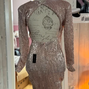 Glittrig champagnefärgad klänning NLY One - Supersnygg glittrig kortklänning från NLY One i champagnefärg med paljetter över hela tyget. Klänningen har lång ärm, figurnära passform och en öppen rygg med pärlknäppning i nacken, (dock är en hake av) Perfekt för dig som vill sticka ut och glänsa.