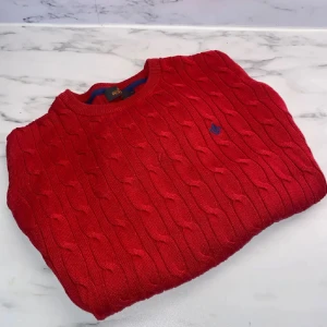 Röd kabelstickad tröja från Morris - Kabelstickad röd tröja från Morris med rund hals och diskret blå logga broderad på bröstet. Tröjan är i mjuk bomull och har lång ärm, perfekt för lager-på-lager under kyliga dagar. Klassisk och stilren design som funkar till allt. 