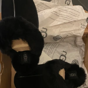 Svarta UGG Disquette tofflor, storlek 39 - Mysiga svarta UGG Disquette tofflor med fluffig päls runt öppningen och ovandel i mocka. Sulan är rejäl och mönstrad för bra grepp. Perfekta för chill hemma eller när du vill ha det extra bekvämt. Klassisk UGG-logga på hälremmen. Kommer med orginalförpackning aldrig använda!