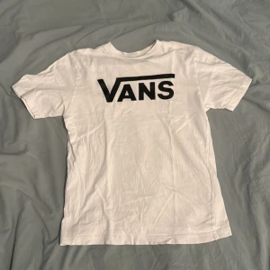 Vit Vans t-shirt med logga - Vit t-shirt från Vans med stor svart logga på bröstet. Klassisk passform och rund halsringning. Tillverkad i mjuk bomull, perfekt för en avslappnad och cool stil.