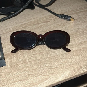 Svarta ovala solglasögon Carin Wester - Snygga svarta solglasögon från Carin Wester med ovala bågar och diskret logga i guld på skalmarna. Glasögonen har en stilren och trendig look som passar perfekt till sommaren. Ramen är i blank plast och ger en cool vibe.