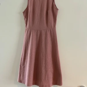 Rosa glittrig kortklänning med v-ringning - Supersöt rosa kortklänning med glittrigt tyg och v-ringad framsida. Ärmlös modell med lätt utställd kjol som ger en fin siluett. Perfekt för dig som vill sticka ut lite extra med en enkel men snygg look. Från H&M. Strl 36. Använd 1 gång. 