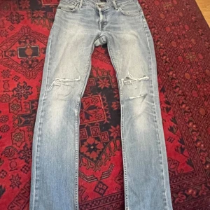 Ljusblå jeans från Tiger of Sweden  - Ljusblå jeans från Tiger of Sweden med slitningar och hål på båda knäna. Klassisk femficksmodell med normal passform. Säljer eftersom de ej kommer till användning💕.                             Midjemått (Tvärs över): 40cm                                                Innerbenslängd: 82cm