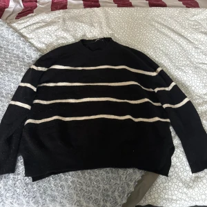 Svart stickad randig tröja - En svart stickad tröja med vita horisontella ränder. Tröjan har en avslappnad passform och långa ärmar, perfekt för lager-på-lager. Mjuk och skön att bära, passar till jeans eller kjol för en chill look.