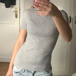 Intimisimi t shirt - En stilren ljusgrå t-shirt med rund hals och korta ärmar. Tillverkad i mjuk bomull som känns skön mot huden. Perfekt att matcha med jeans eller shorts för en clean och enkel look.