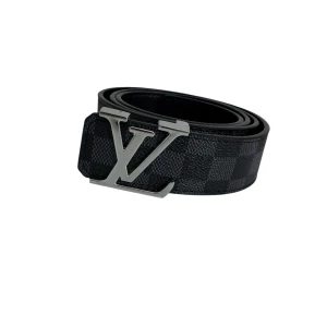 Louis Vuitton svart rutigt bälte - Svart bälte från Louis Vuitton med klassiskt rutigt Damier-mönster och stor LV-logga i silverfärgad metall som spänne. Tillverkat i exklusivt skinn med präglad logotyp på insidan. Perfekt accessoar för att lyfta din outfit.