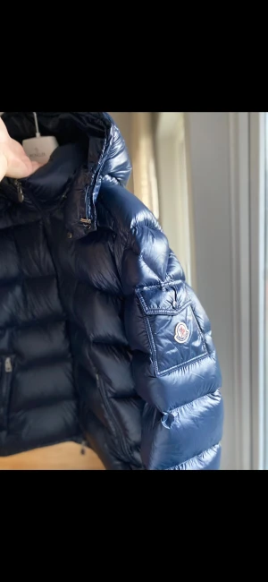 Mörkblå Moncler pufferjacka - Snygg mörkblå pufferjacka från Moncler med glansig finish och klassisk logga på ärmen. Jackan har hög krage, dragkedja framtill och praktiska fickor med zip. Perfekt för kalla dagar och har en riktigt schysst streetstil. NFC-Scan finns vid moncler märket och Kalle anka på insidan. Skicka dm vid fler bilder eller frågor😊
