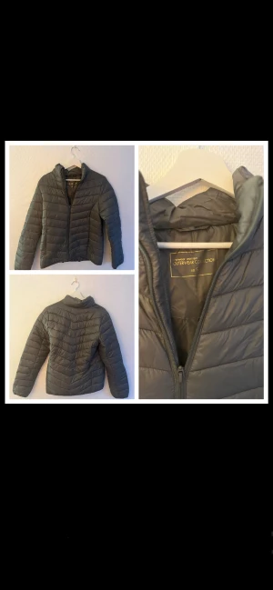 Mörkgrå/grön pufferjacka från Mywear - Säljer en stilren mörkgrön pufferjacka från Mywear i storlek S. Jackan har quiltad design, hög krage och dragkedja framtill. Perfekt för dig som gillar en clean look och vill hålla dig varm under kyliga dagar.