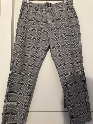Rutigta kostymbyxor från Bershka - Snygga kostymbyxor från Bershka med grå, svart och rosa rutor. Byxorna har normal passform, bälteshällor och klassisk knappstängning. Perfekt för dig som gillar en stilren och trendig look med lite edge.