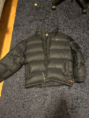 Svart Nike pufferjacka L - Hej! säljer en billig Nike jacka som är lite old school men den har en trasig dragkedja så därför är det så billigt