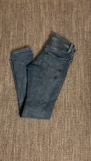 jack&jones jeans med slitningar - Snygga blå jeans från Jack & Jones i storlek 28/30 och i modellen Slim/Glenn. De har slitna detaljer och hål på benen för en cool, avslappnad look. Klassisk femficksdesign och smal passform som sitter tajt längs benen. Perfekta för dig som gillar streetstyle. 