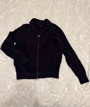 Mörkblå Massimo Dutti kofta - Mörkblå kofta från Massimo Dutti med hel dragkedja framtill och ribbade muddar. Tröjan har en klassisk krage och är långärmad, perfekt för dig som gillar stilrena och enkla plagg. Materialet känns mjukt och är troligtvis bomull eller ull. Använd men i gott skick. Storlek M