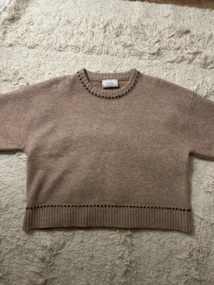 Beige stickad tröja från Neo Noir - Säljer en beige stickad tröja från Neo Noir med svarta broderade detaljer vid halsringning och nederkant. Perfekt för dig som gillar stilrena och mysiga plagg med en twist.🫰🏼💗