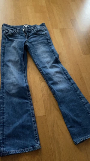 Blå bootcut jeans från Gina Tricot - Snygga blå jeans från Gina Tricot i storlek 158. Modellen har klassisk bootcut med utsvängda ben och fem fickor, inklusive bakfickor med lock och knapp. Jeansen är tillverkade i jeansmaterial och har normal passform.