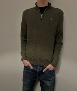 Olivgrön stickad tröja med half zip - Snygg olivgrön stickad tröja från Morris med half zip och liten broderad logga på bröstet. Tröjan har långärmad passform, ribbade muddar och en klassisk krage. Perfekt för dig som gillar stilrena och bekväma plagg. Använd endast några gånger! 