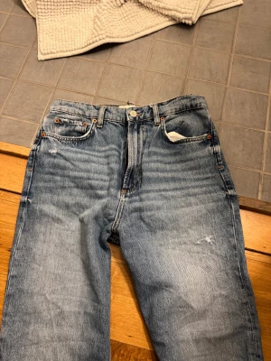 Blå raka jeans från Zara, strl 36 - Snygga blå jeans från Zara i storlek 36 med raka ben och slitna detaljer på låren och knäet. Klassisk femficksmodell med knapp och dragkedja framtill. Jeansen har en cool, vintage tvätt och är tillverkade i bomull.