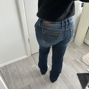 Replay blå lågmidjade jeans - Säljer ett par snygga blå jeans från Replay i modellen Jennpez. Jeansen har coola dragkedjedetalj på bakfickan, låg midja och raka ben. Innerbebslängd 80