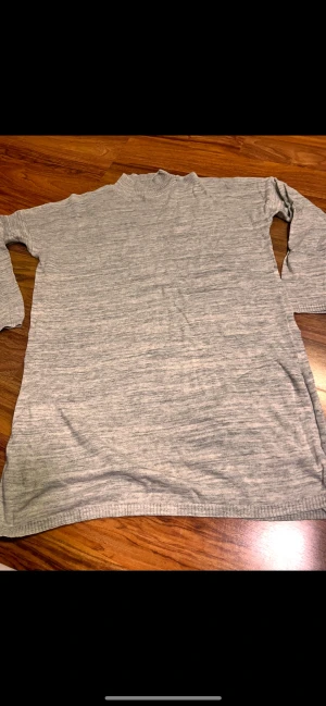 Grå polotröja från C, storlek M - Snygg grå polotröja från C i storlek M. Tröjan har en ribbad hög krage och är långärmad med ribbade muddar vid ärmslut och nederkant. Materialet är mjukt och stickat, perfekt för kyliga dagar. Enkel och clean look som funkar till jeans eller dressade byxor.